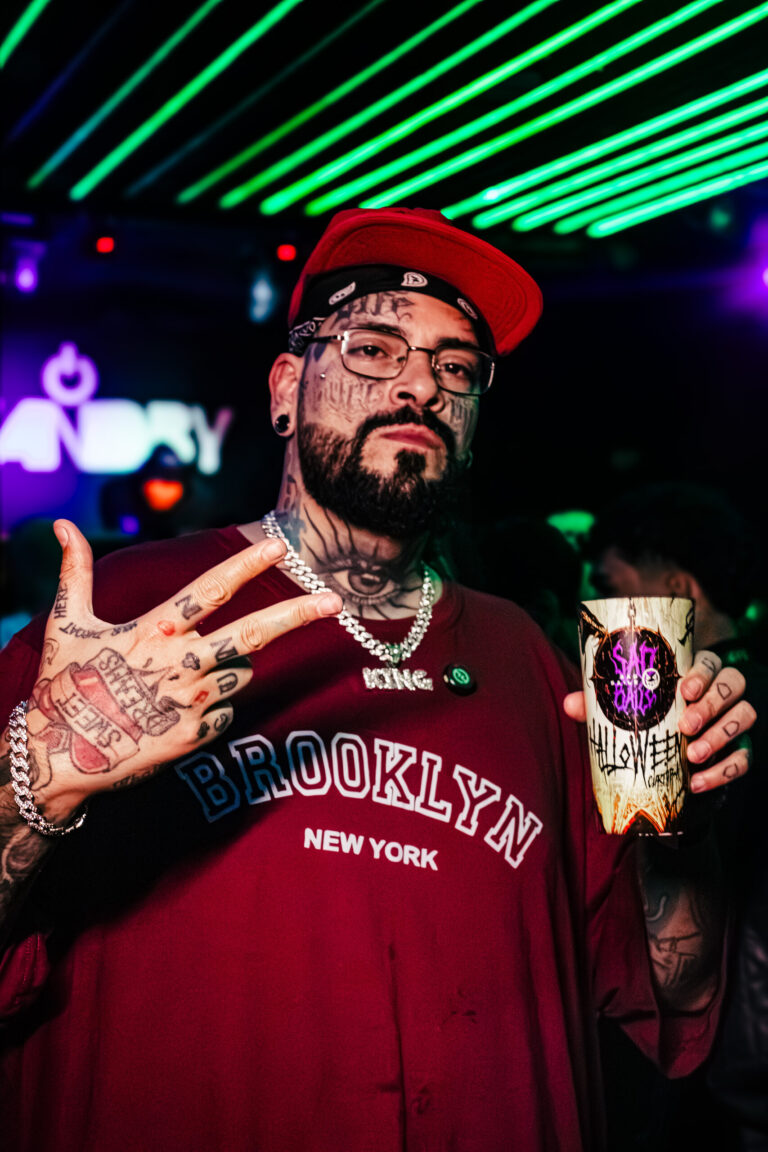 Rapaz tatuado segura copo da Sad Baile e faz sinal com a mão — Sad Baile Curitiba Halloween, 10/10/2026