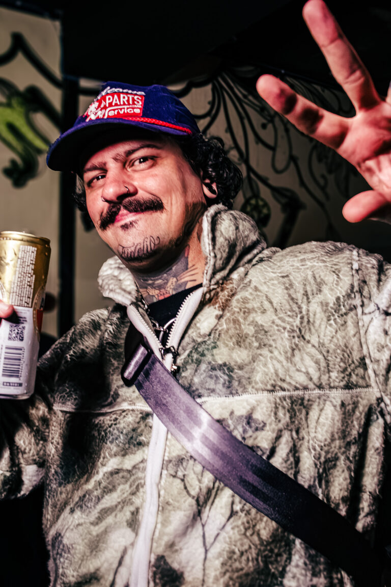 Rapaz de boné e jaqueta camuflada faz sinal com a mão — Sad Baile Curitiba Halloween, 10/10/2026
