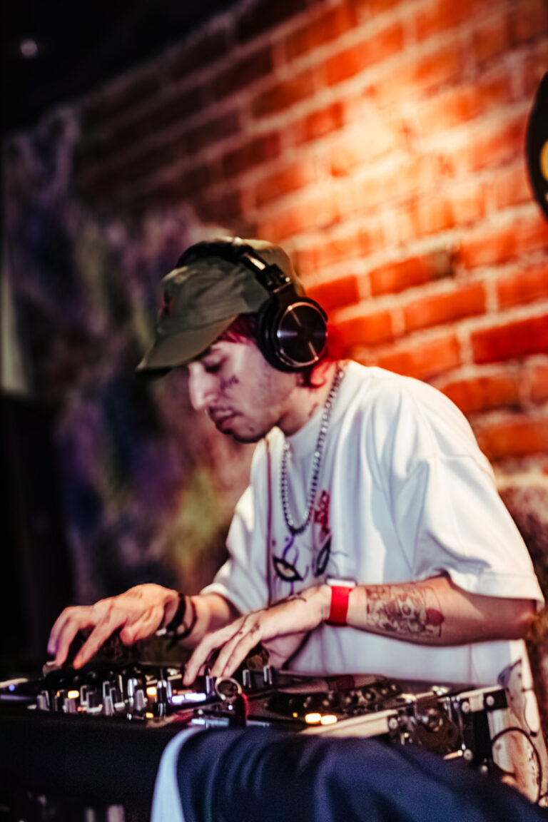 DJ de boné e fones toca em frente aos tijolos — Sad Baile Curitiba Halloween, 10/10/2026