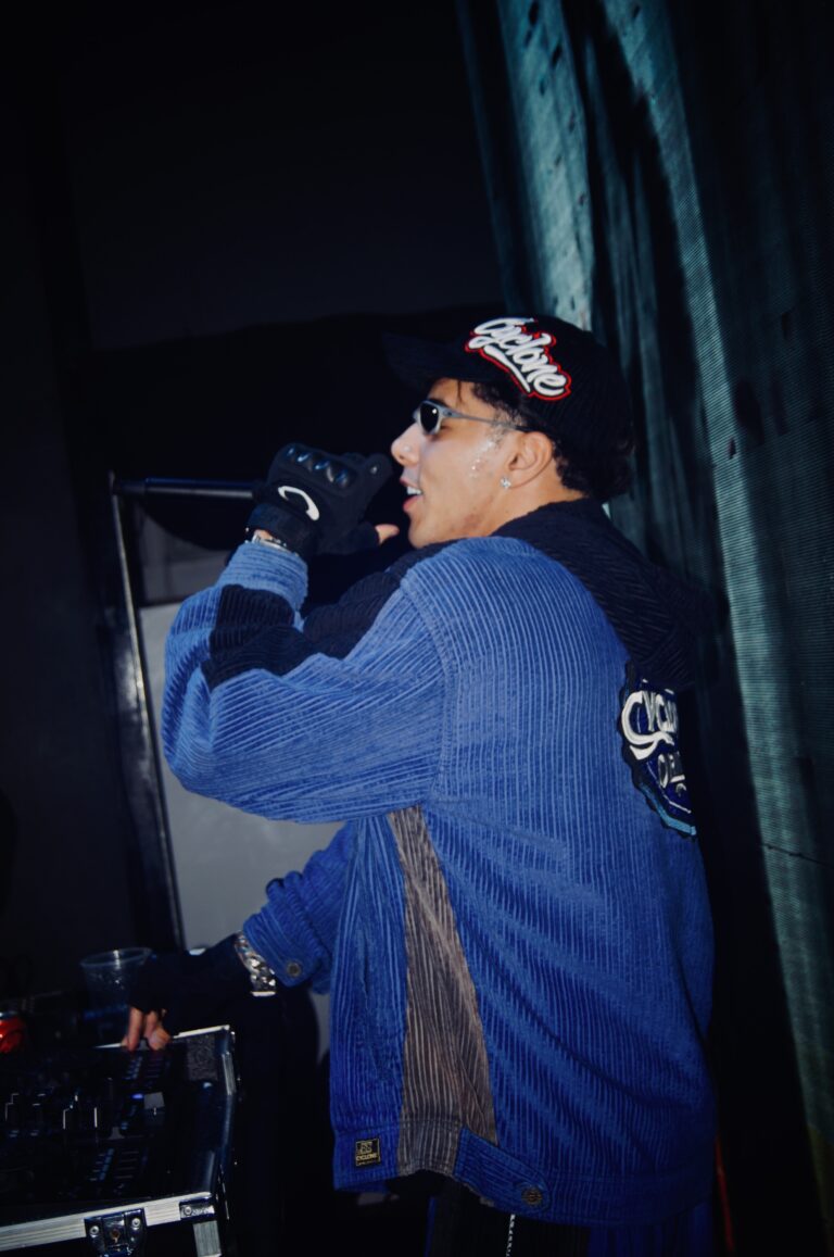 DJ de boné canta no microfone atrás da mesa — Sad Baile Joker, Halloween em São Paulo, 17/10/2026