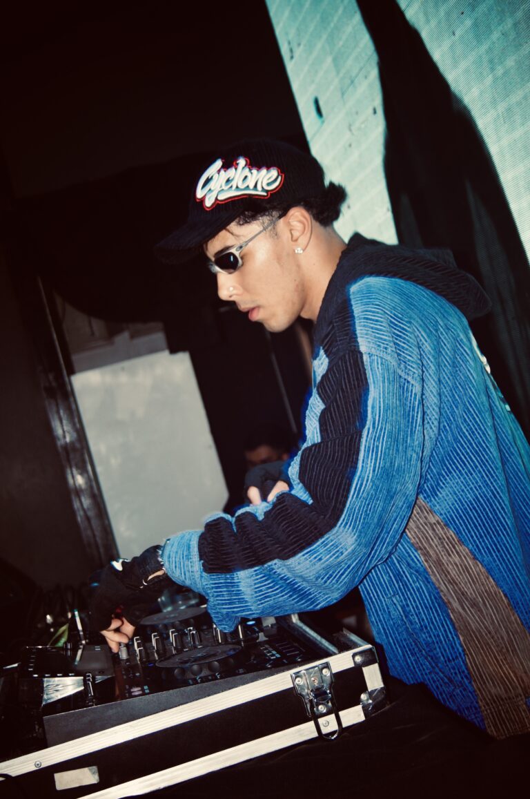 DJ de jaqueta azul nos controles sob luz branca — Sad Baile Joker, Halloween em São Paulo, 17/10/2026