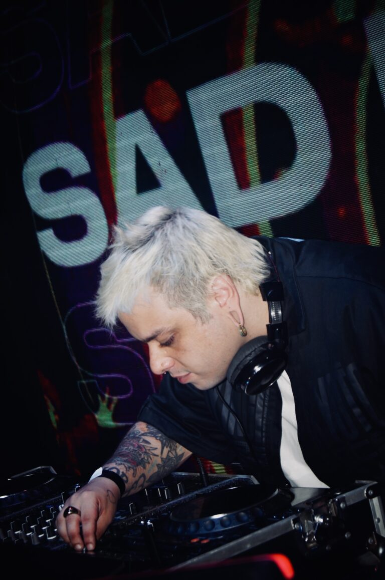 DJ de cabelo platinado com o letreiro Sad ao fundo — Sad Baile Joker, Halloween em São Paulo, 17/10/2026
