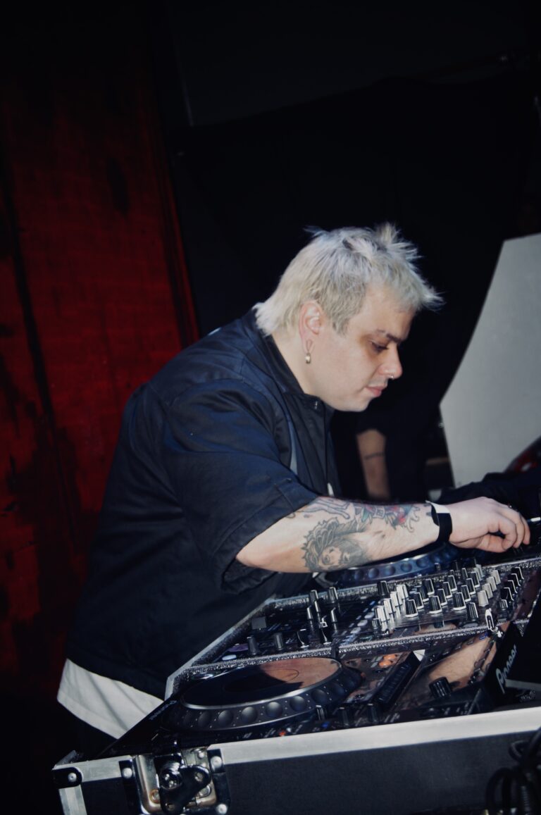 DJ de cabelo platinado toca sob luz vermelha — Sad Baile Joker, Halloween em São Paulo, 17/10/2026