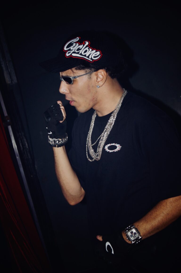 Rapper de boné e correntes cobre a boca com a mão — Sad Baile Joker, Halloween em São Paulo, 17/10/2026