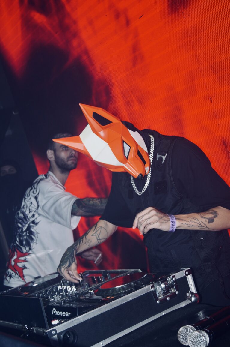 DJ mascarado e amigo diante do telão em chamas — Sad Baile Joker, Halloween em São Paulo, 17/10/2026