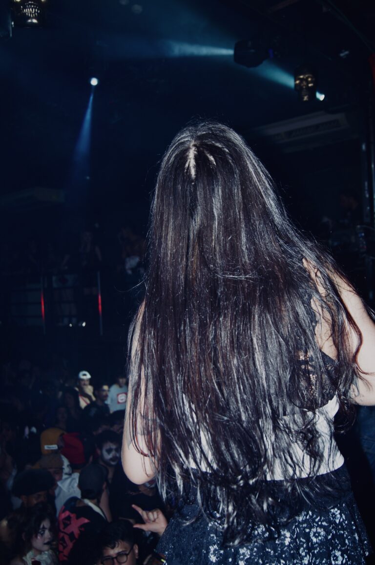 Garota de cabelo comprido de costas olha a pista — Sad Baile Joker, Halloween em São Paulo, 17/10/2026