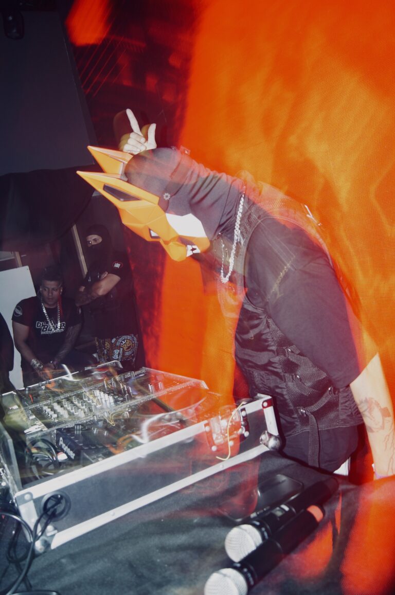 DJ de máscara de raposa faz sinal de paz sob luz laranja — Sad Baile Joker, Halloween em São Paulo, 17/10/2026