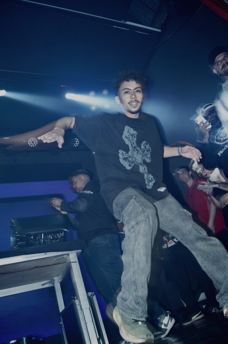 Artista de camiseta com cruz sorri no palco — Sad Baile Joker, Halloween em São Paulo, 17/10/2026