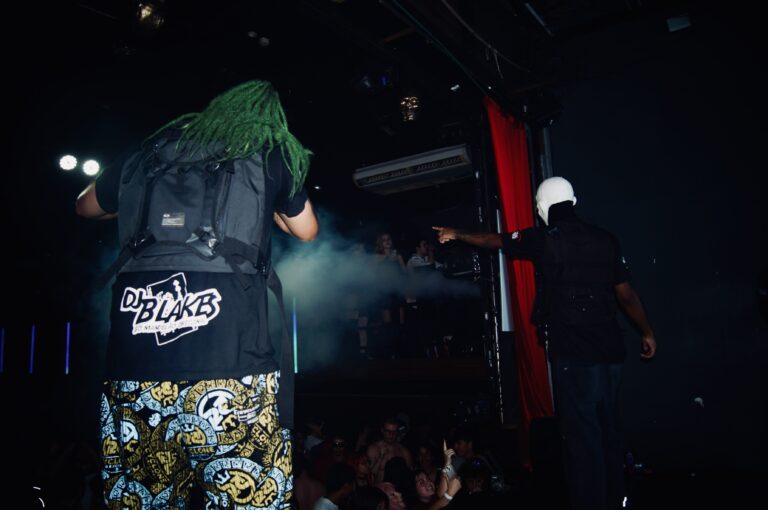Artista de peruca verde de costas para a câmera — Sad Baile Joker, Halloween em São Paulo, 17/10/2026