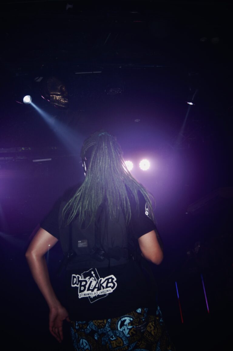 Artista de peruca verde de costas sob luz roxa — Sad Baile Joker, Halloween em São Paulo, 17/10/2026