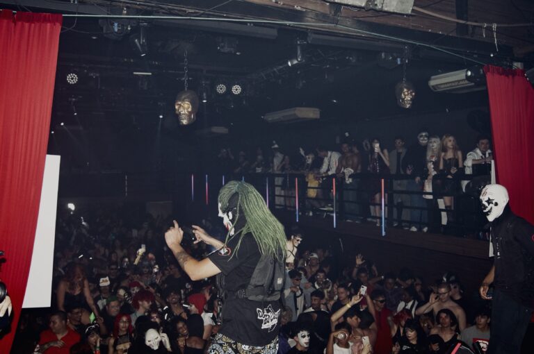 Artista de peruca verde no palco diante da pista lotada, em outro ângulo — Sad Baile Joker, Halloween em São Paulo, 17/10/2026