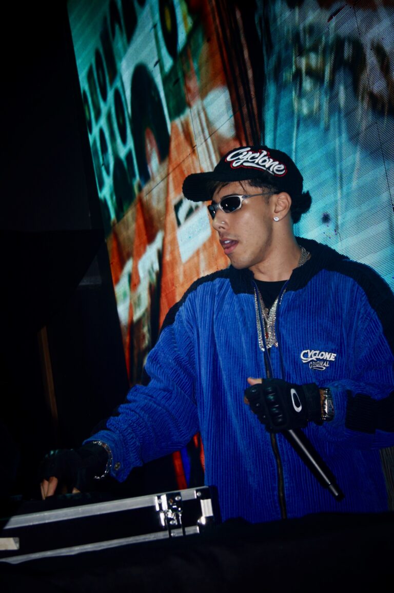 DJ de jaqueta azul diante do telão colorido — Sad Baile Joker, Halloween em São Paulo, 17/10/2026