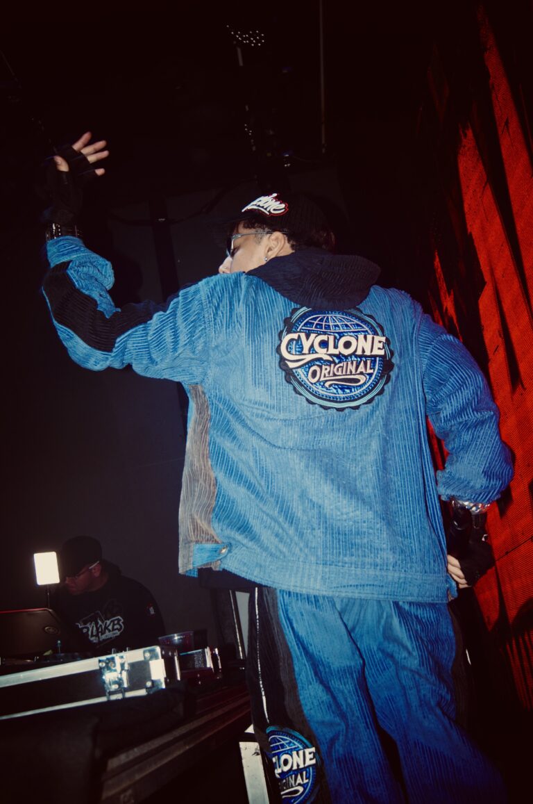 DJ de jaqueta azul de costas sob luz vermelha — Sad Baile Joker, Halloween em São Paulo, 17/10/2026