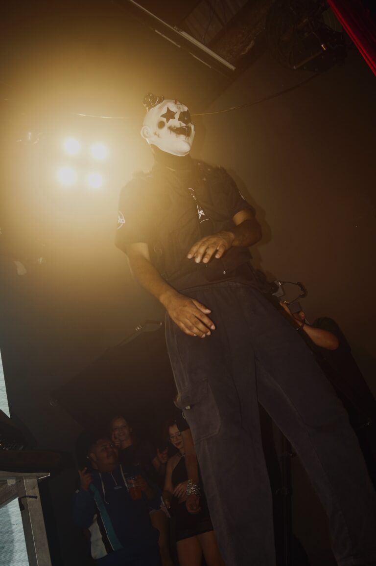 Artista de máscara branca sob luz amarela — Sad Baile Joker, Halloween em São Paulo, 17/10/2026