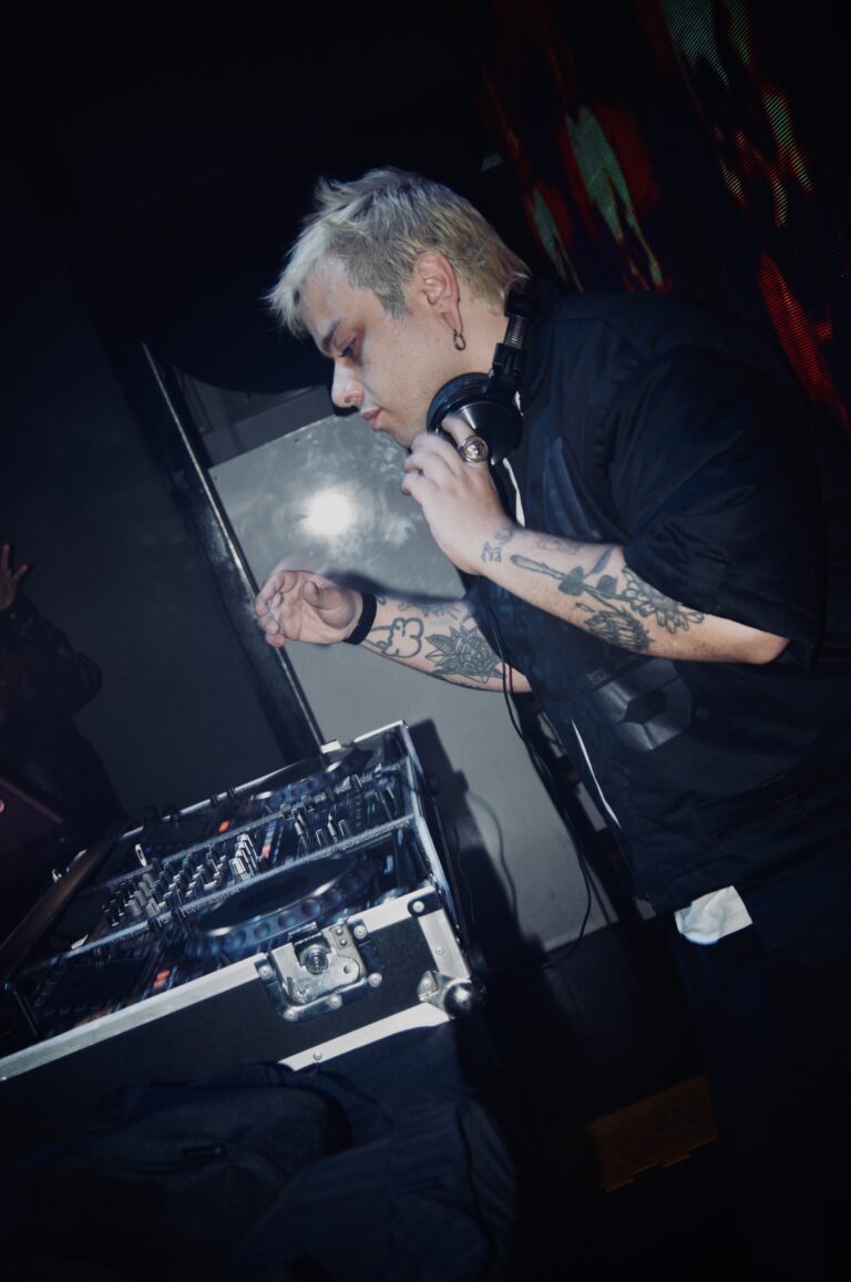 DJ de cabelo platinado nos controles sob luz branca — Sad Baile Joker, Halloween em São Paulo, 17/10/2026