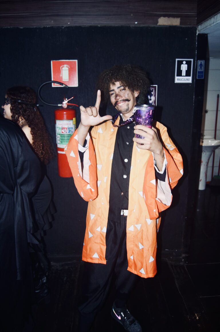 Rapaz de kimono laranja faz sinal de rock — Sad Baile Joker, Halloween em São Paulo, 17/10/2026
