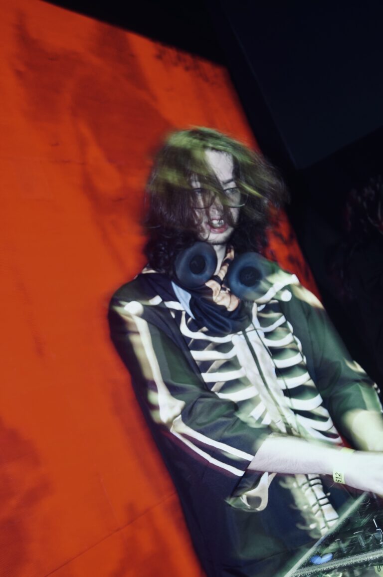 DJ de jaqueta de esqueleto diante do telão laranja — Sad Baile Joker, Halloween em São Paulo, 17/10/2026