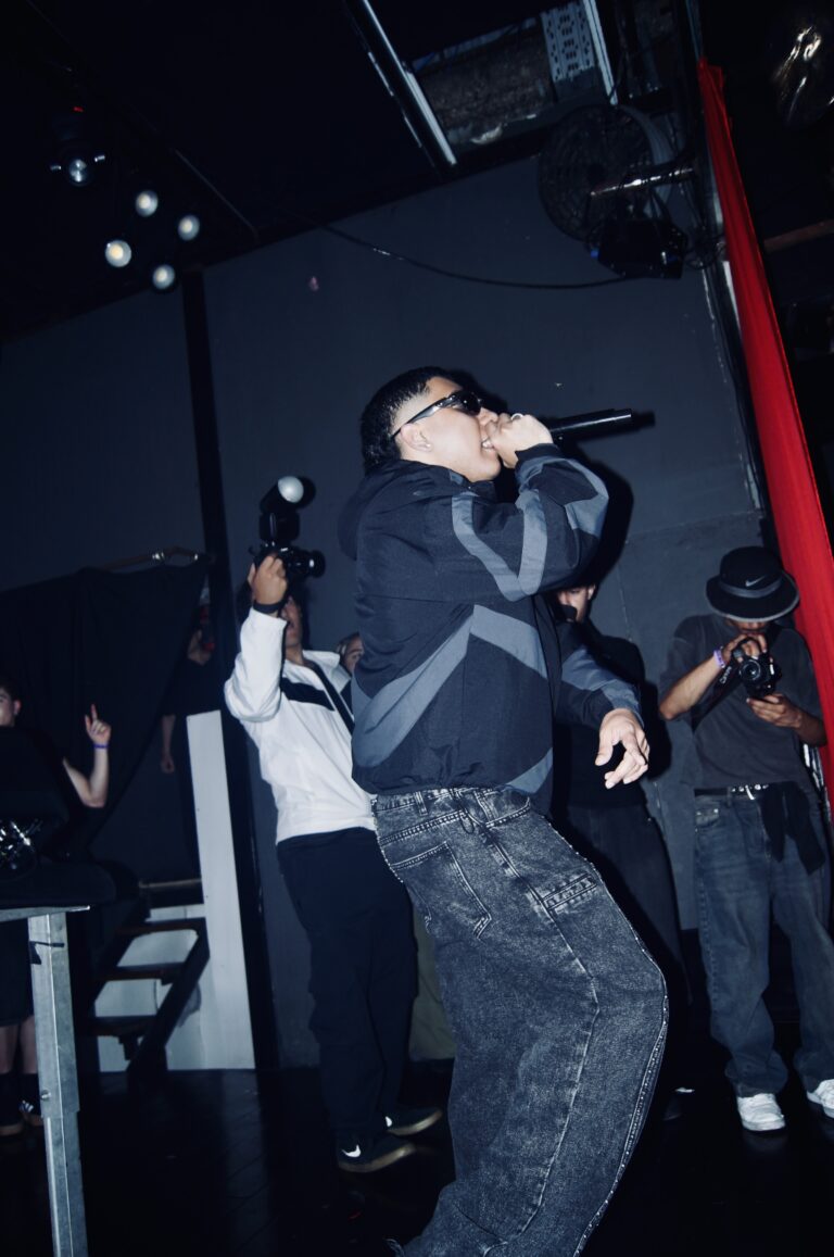 Rapper canta ao microfone com fotógrafos ao lado — Sad Baile Joker, Halloween em São Paulo, 17/10/2026