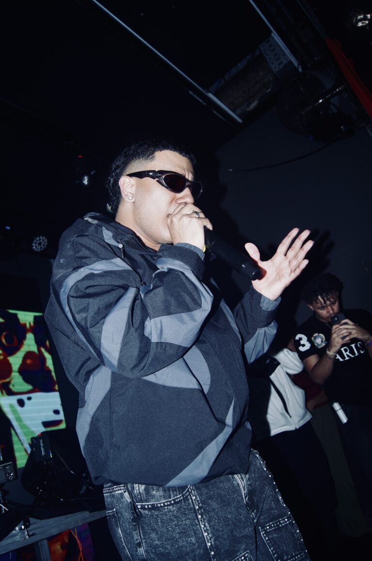 Rapper de óculos escuros faz gesto com a mão — Sad Baile Joker, Halloween em São Paulo, 17/10/2026