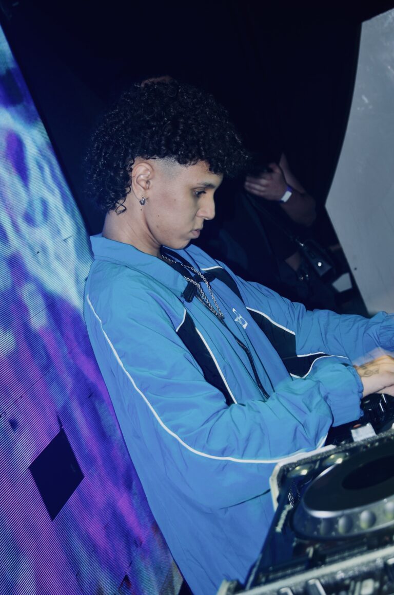DJ de cabelo cacheado diante do telão roxo — Sad Baile Joker, Halloween em São Paulo, 17/10/2026