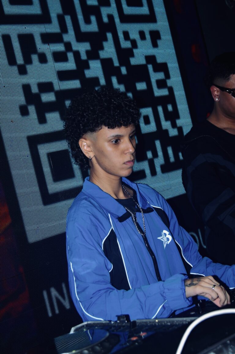 DJ de cabelo cacheado concentrado diante do QR code — Sad Baile Joker, Halloween em São Paulo, 17/10/2026