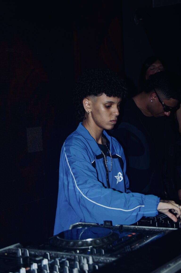 DJ de jaqueta azul nos controles com fundo escuro — Sad Baile Joker, Halloween em São Paulo, 17/10/2026