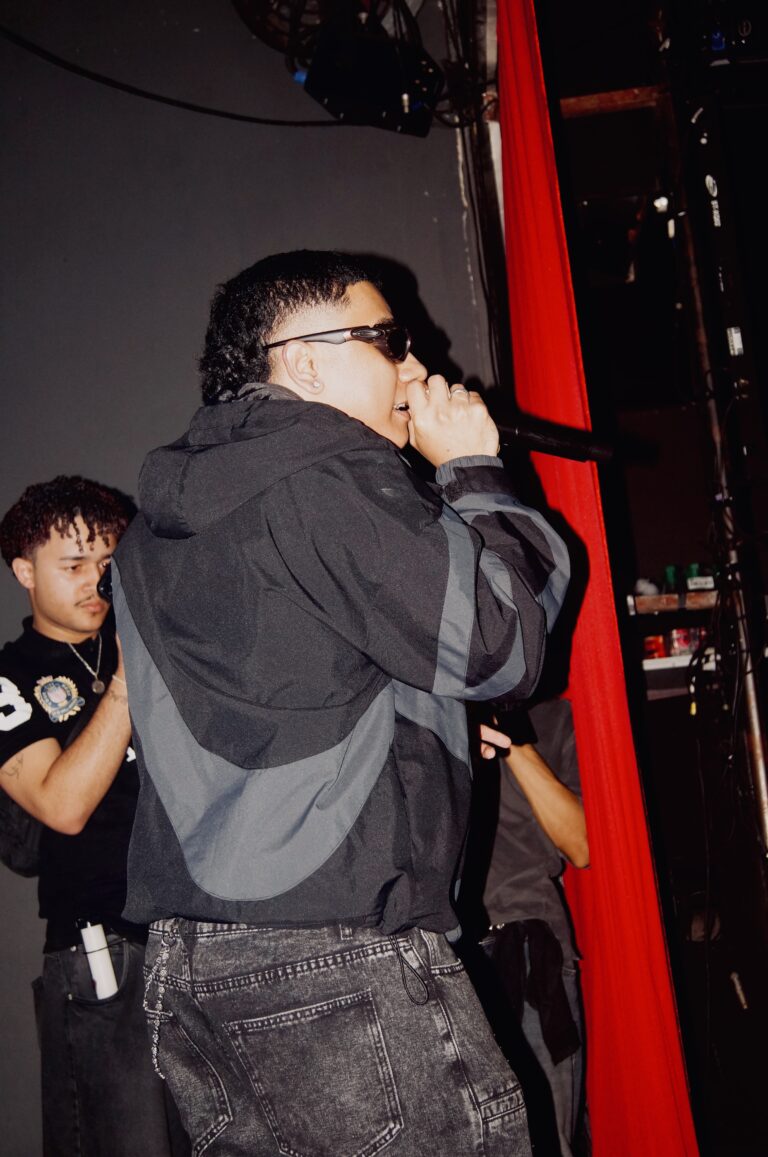 Rapper de jaqueta cinza canta junto à cortina vermelha — Sad Baile Joker, Halloween em São Paulo, 17/10/2026