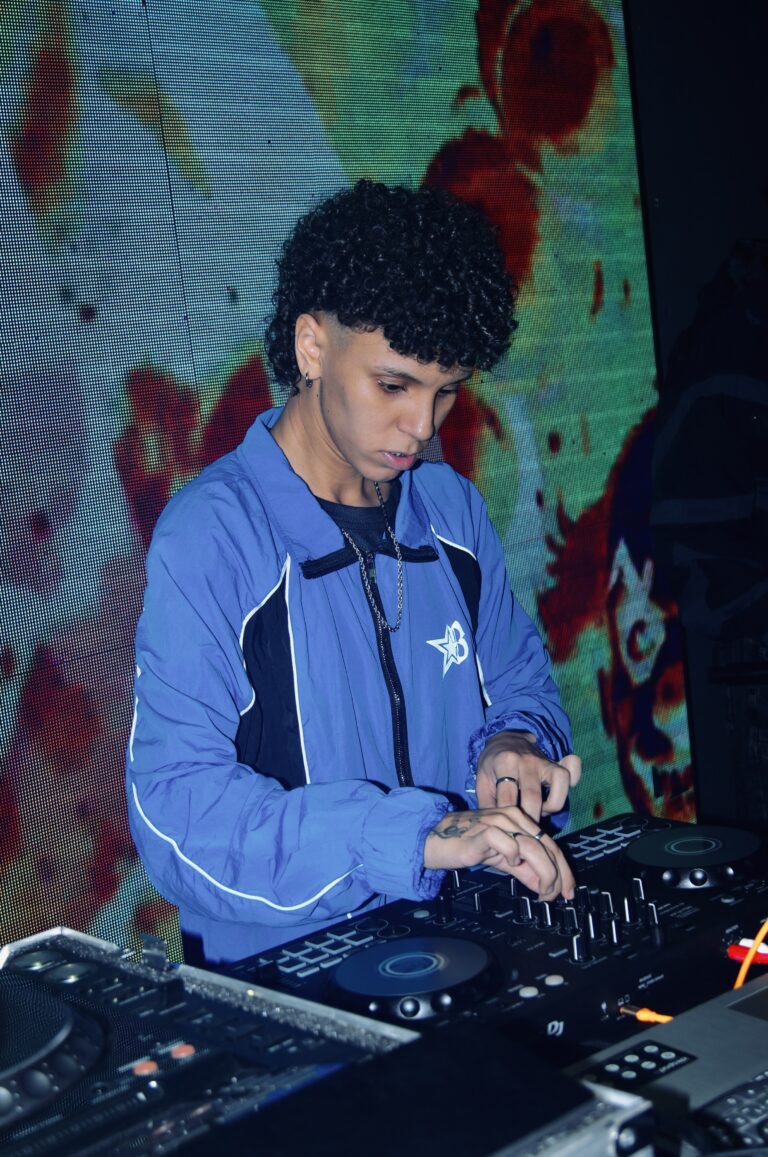 DJ de jaqueta azul diante do telão florido — Sad Baile Joker, Halloween em São Paulo, 17/10/2026