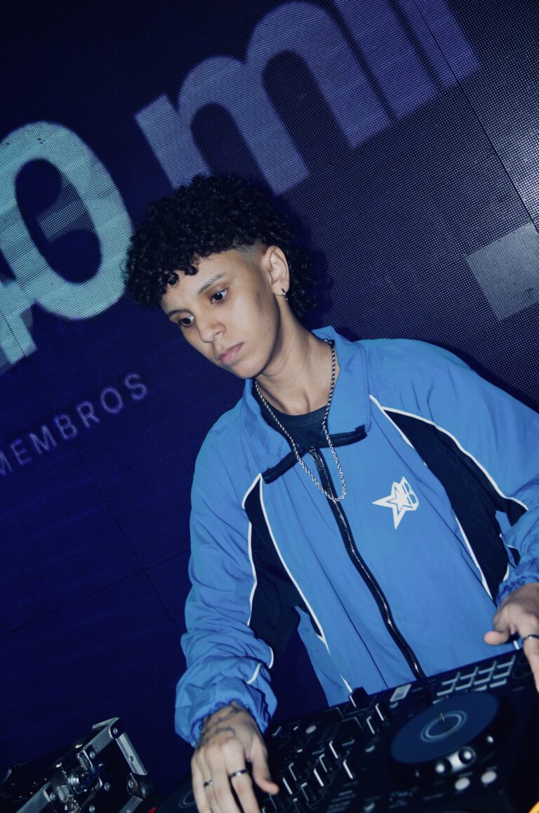 DJ de cabelo cacheado diante do telão com texto — Sad Baile Joker, Halloween em São Paulo, 17/10/2026