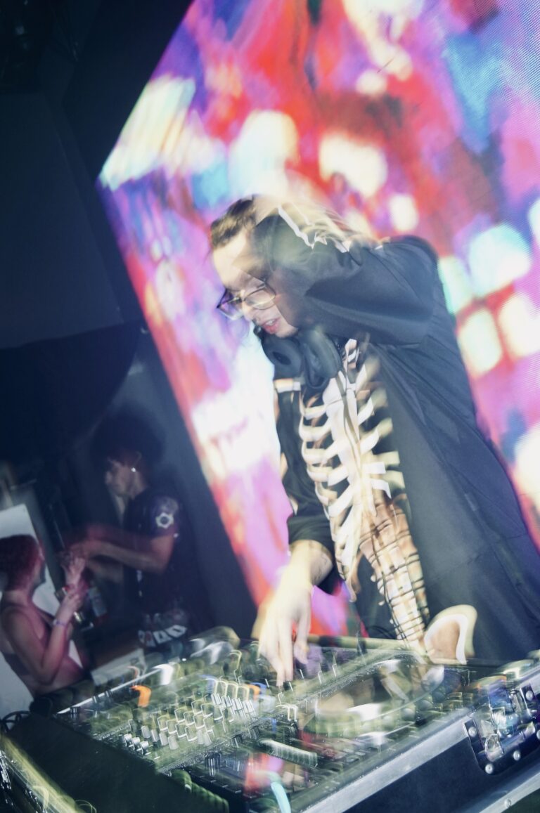 DJ de óculos e jaqueta de ossos mixando sob luzes coloridas — Sad Baile Joker, Halloween em São Paulo, 17/10/2026