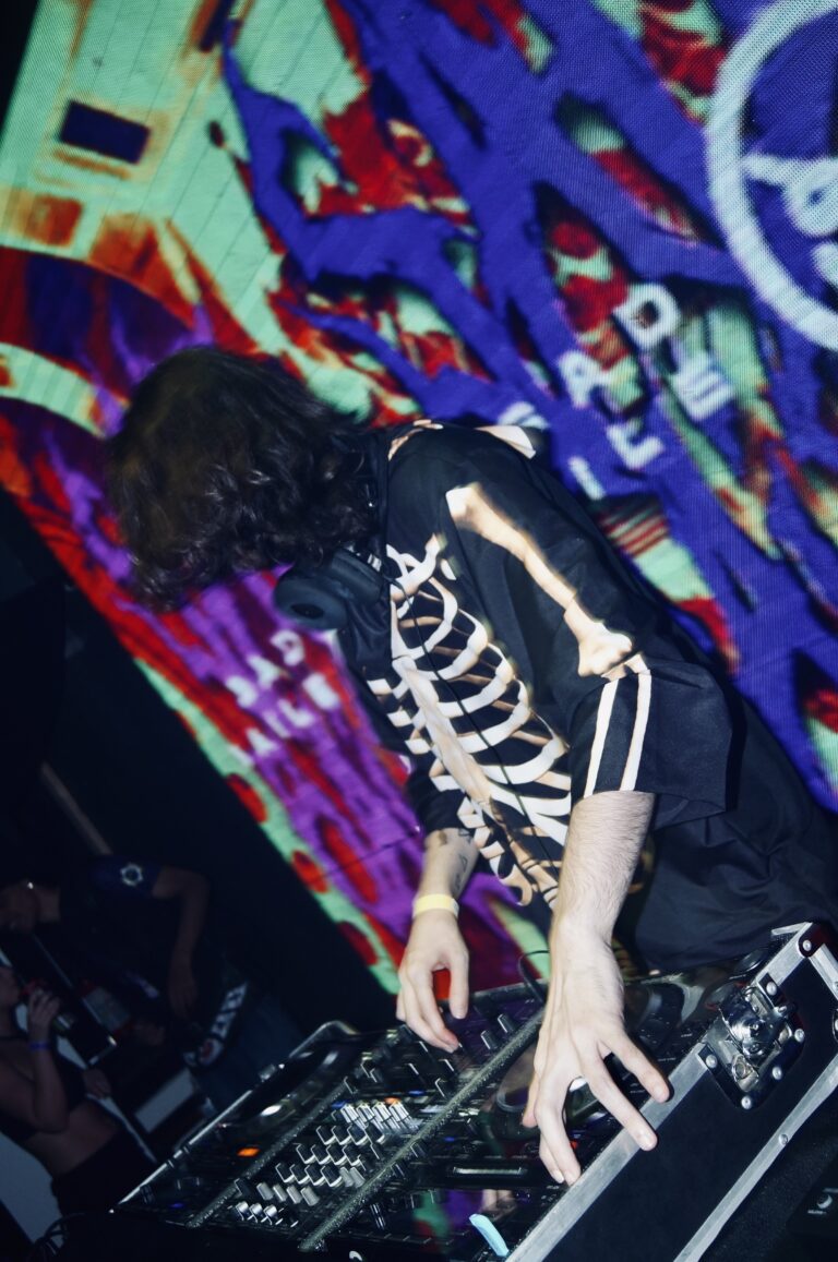 DJ de jaqueta de esqueleto diante do telão grafitado — Sad Baile Joker, Halloween em São Paulo, 17/10/2026