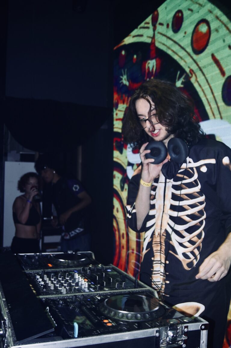 DJ de jaqueta de esqueleto fala ao celular na cabine — Sad Baile Joker, Halloween em São Paulo, 17/10/2026