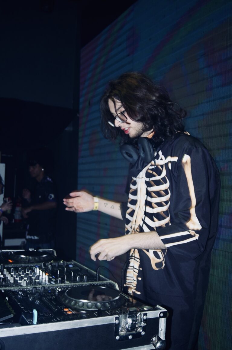 DJ de óculos sorri com o telão azul ao fundo — Sad Baile Joker, Halloween em São Paulo, 17/10/2026
