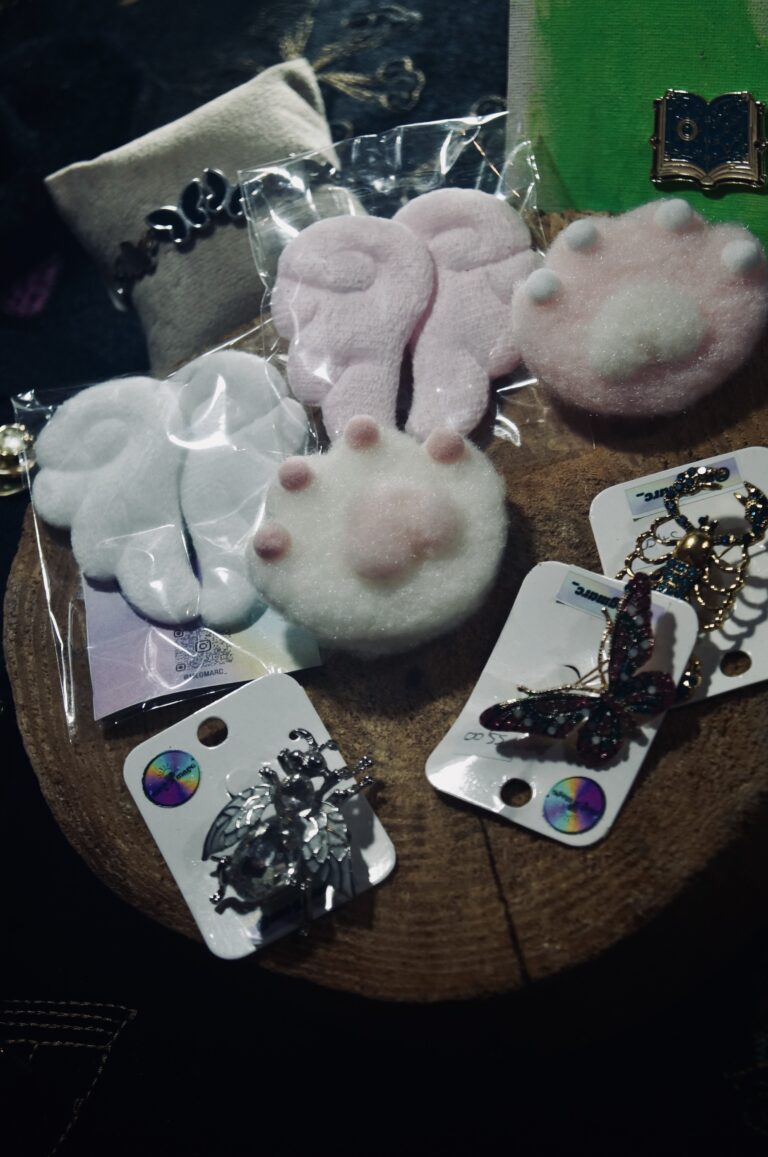 Pelúcias e acessórios na mesa de expositor — Sad Baile Joker, Halloween em São Paulo, 17/10/2026