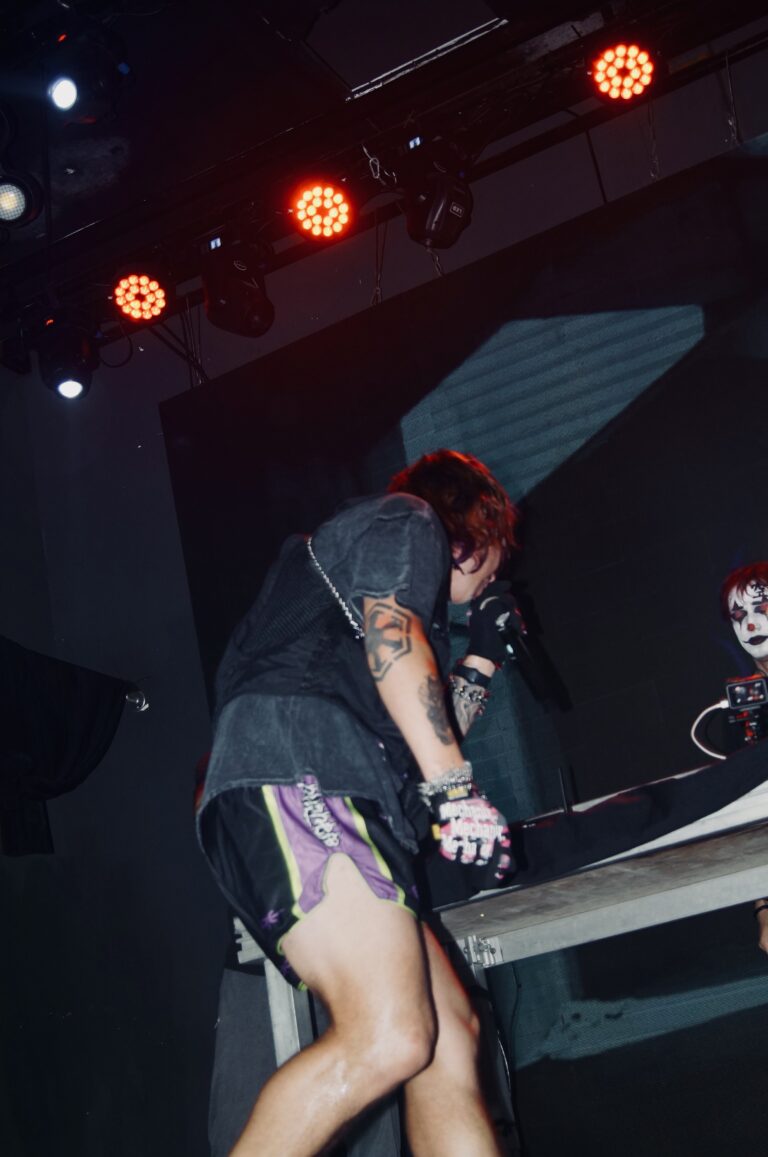 Artista de shorts se apoia na mesa do palco — Sad Baile Joker, Halloween em São Paulo, 17/10/2026