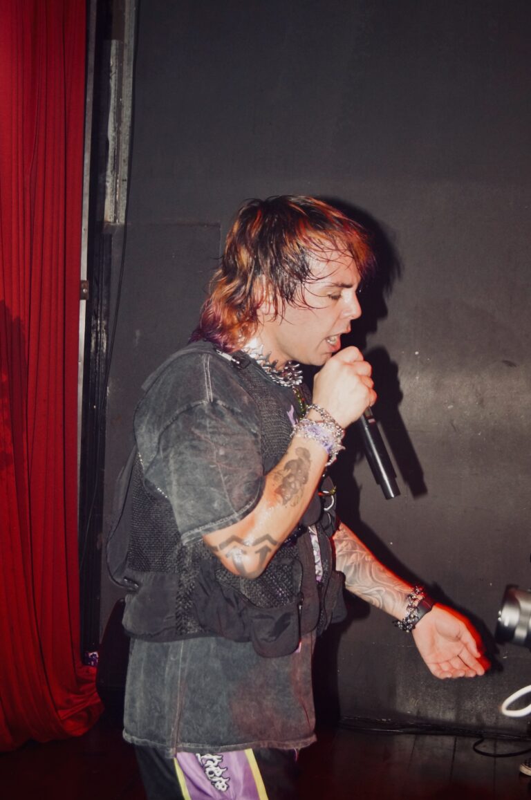 Artista de cabelo ruivo canta ao microfone — Sad Baile Joker, Halloween em São Paulo, 17/10/2026