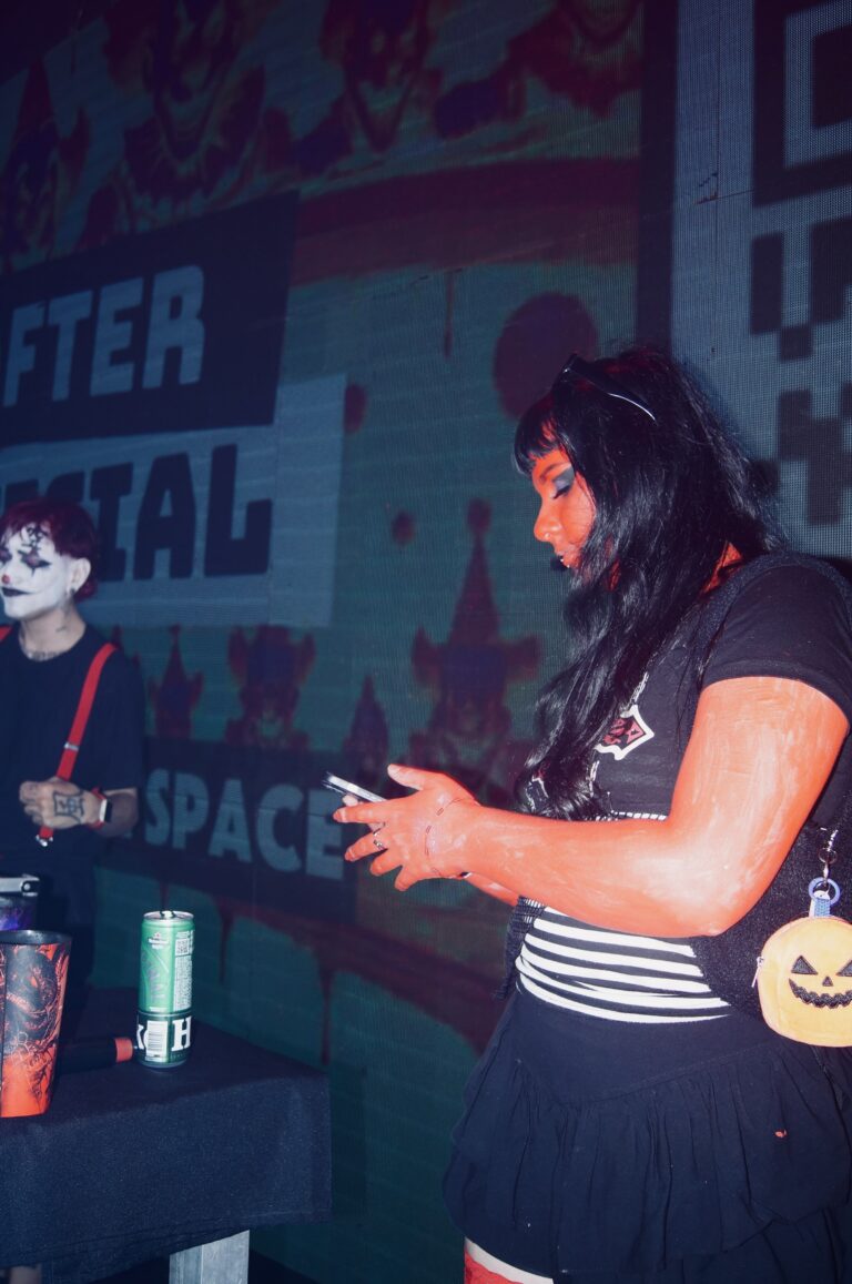Garota de blusa listrada com abóbora na cintura usa o celular — Sad Baile Joker, Halloween em São Paulo, 17/10/2026