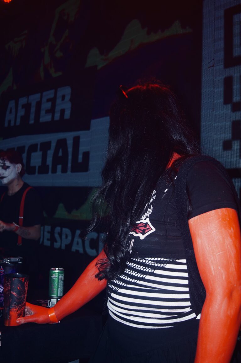 Garota de maquiagem laranja diante do telão — Sad Baile Joker, Halloween em São Paulo, 17/10/2026
