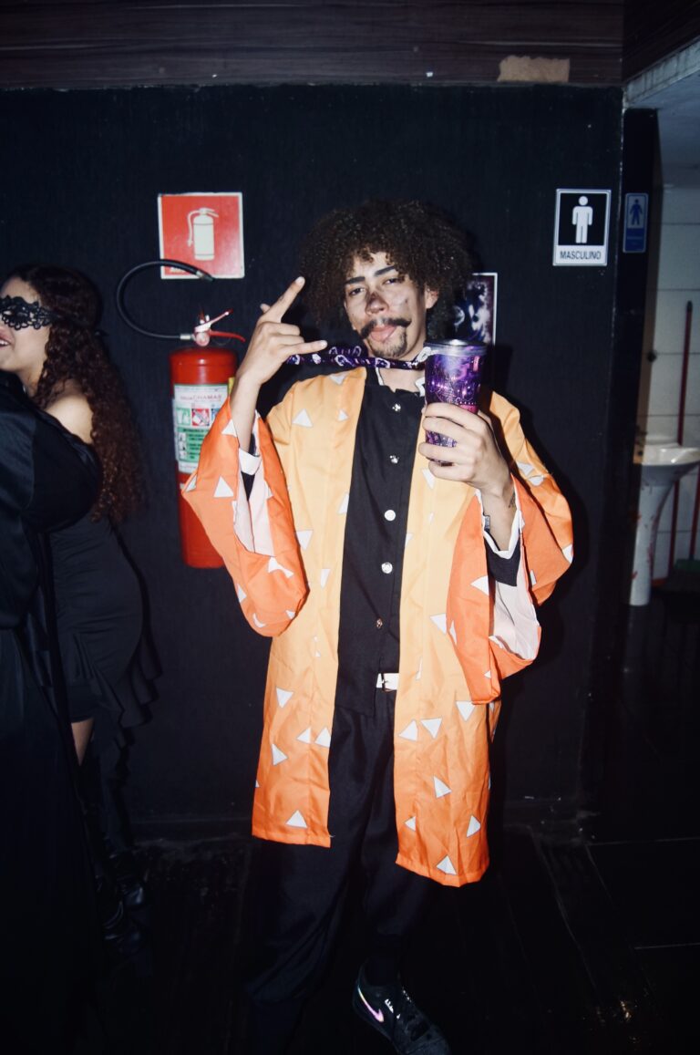 Rapaz de kimono laranja faz pose junto à parede — Sad Baile Joker, Halloween em São Paulo, 17/10/2026
