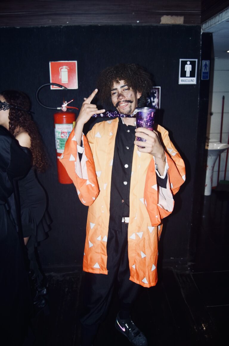 Rapaz de kimono laranja faz careta com copo na mão — Sad Baile Joker, Halloween em São Paulo, 17/10/2026