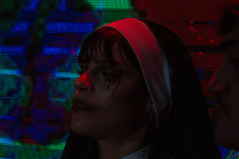 Freira de perfil diante do telão colorido — Sad Baile Joker, Halloween em São Paulo, 17/10/2026
