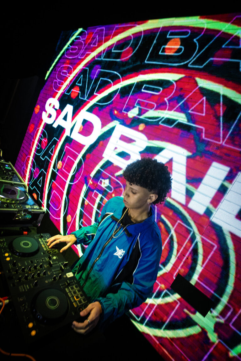 DJ toca diante do logo da Sad Baile em neon — Sad Baile Joker, Halloween em São Paulo, 17/10/2026