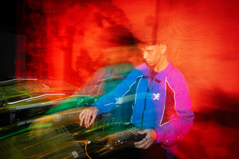 DJ de jaqueta azul sob luz vermelha — Sad Baile Joker, Halloween em São Paulo, 17/10/2026