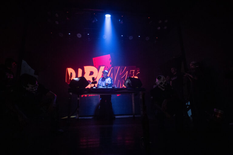 Palco com letreiro em neon visto de longe — Sad Baile Joker, Halloween em São Paulo, 17/10/2026