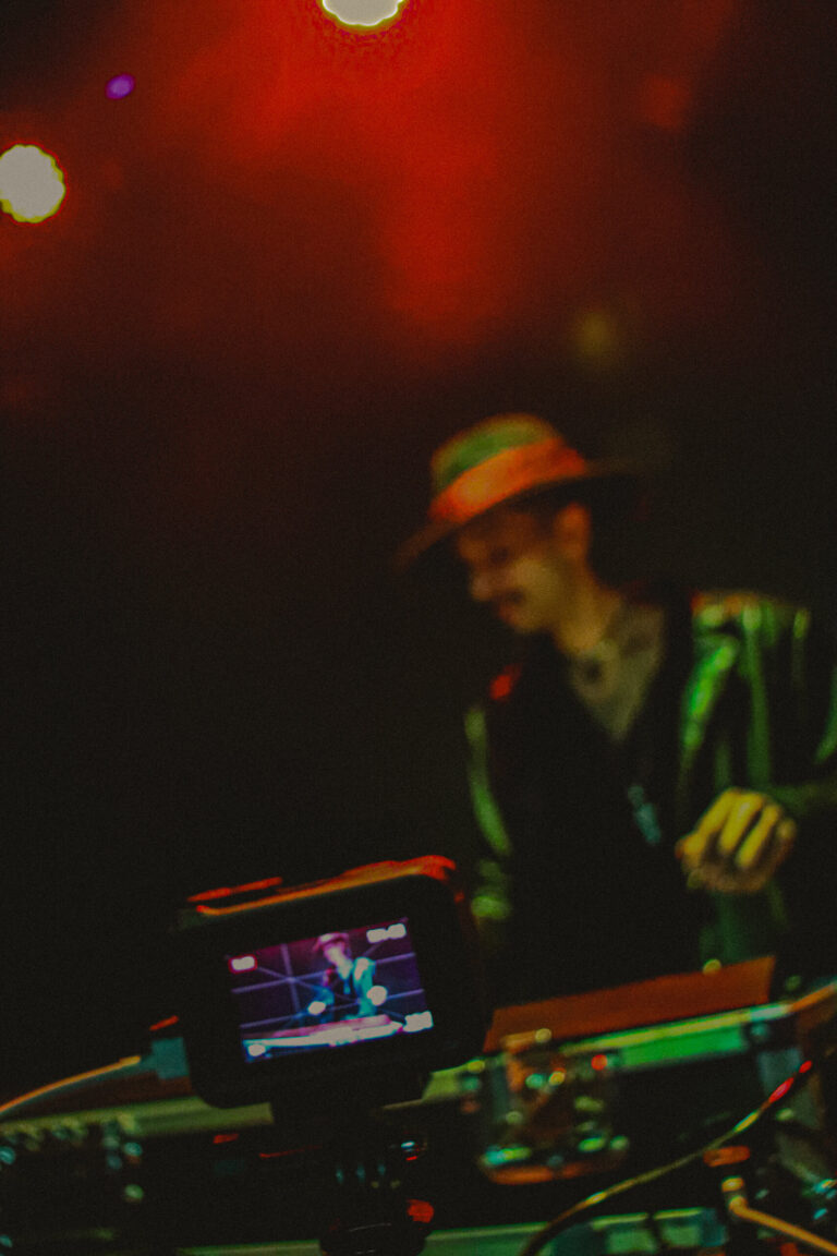 DJ de chapéu e jaqueta verde mixando sob luz vermelha — Sad Baile Joker, Halloween em São Paulo, 17/10/2026