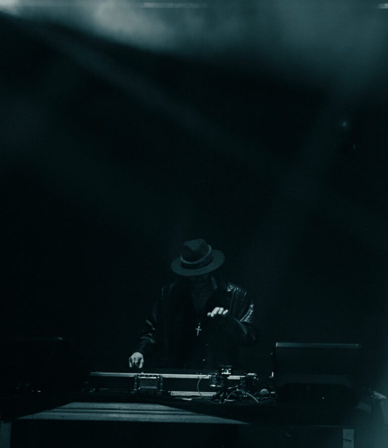Silhueta do DJ de chapéu sob luz azulada fria — Sad Baile Joker, Halloween em São Paulo, 17/10/2026
