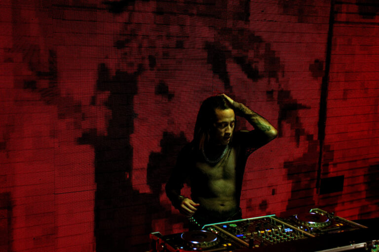 DJ ajeita o cabelo na cabine diante do telão vermelho — Sad Baile Joker, Halloween em São Paulo, 17/10/2026