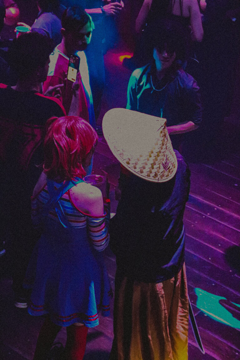 Pista com fantasias coloridas e chapéu de palha em primeiro plano — Sad Baile Joker, Halloween em São Paulo, 17/10/2026