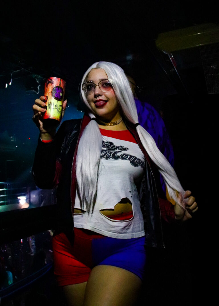 Convidada fantasiada de Arlequina dança com lata na mão — Sad Baile Joker, Halloween em São Paulo, 17/10/2026