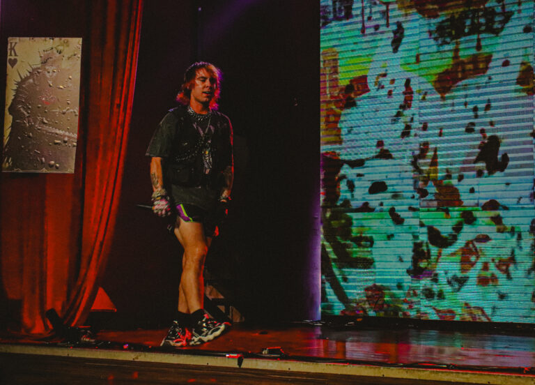 Artista atravessa o palco entre a cortina vermelha e o telão — Sad Baile Joker, Halloween em São Paulo, 17/10/2026